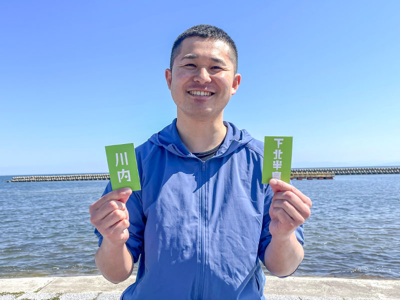 むつ市地域おこし協力隊の圓山遊夢さんが海辺で笑顔を見せる様子